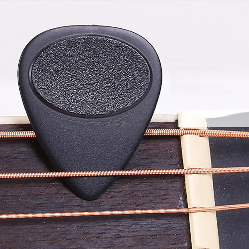 A close-up view of a black non-slip nylon guitar pick resting on a wooden fretboard.