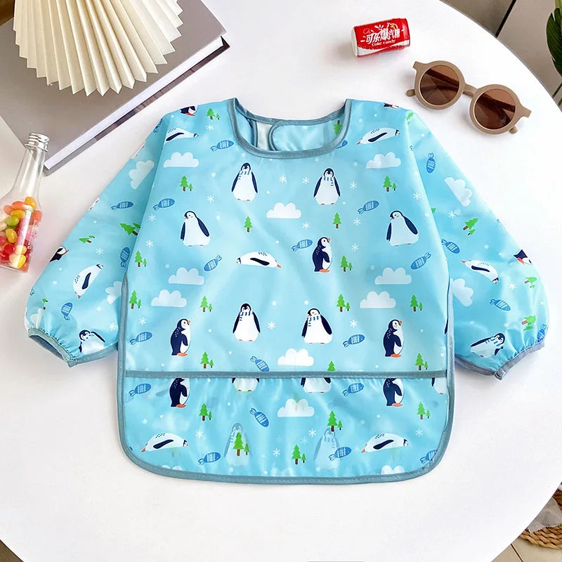 Light blue full-sleeve waterproof baby bib featuring a cute cartoon design of penguins and clouds