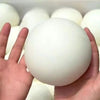 A hand is holding a large, white squishy bread stress ball with other similar balls in the background.