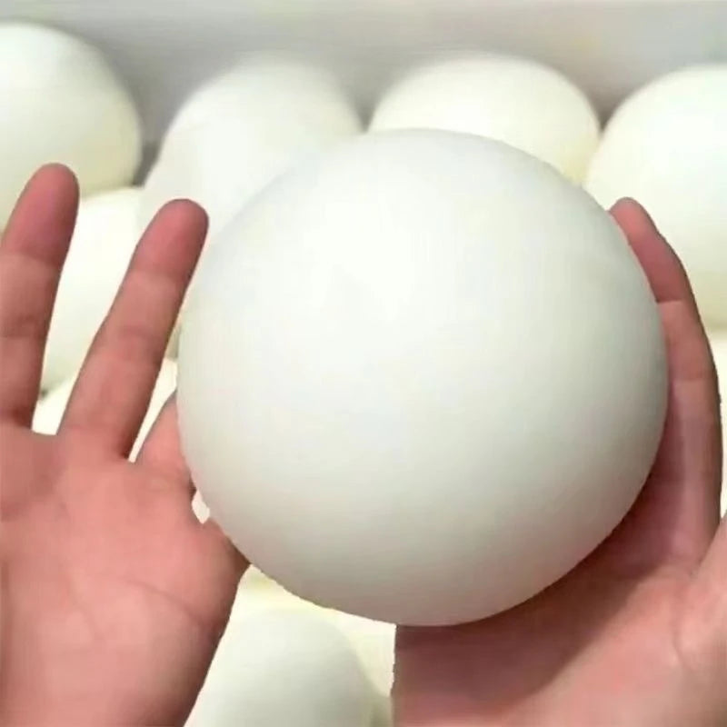 A hand is holding a large, white squishy bread stress ball with other similar balls in the background.