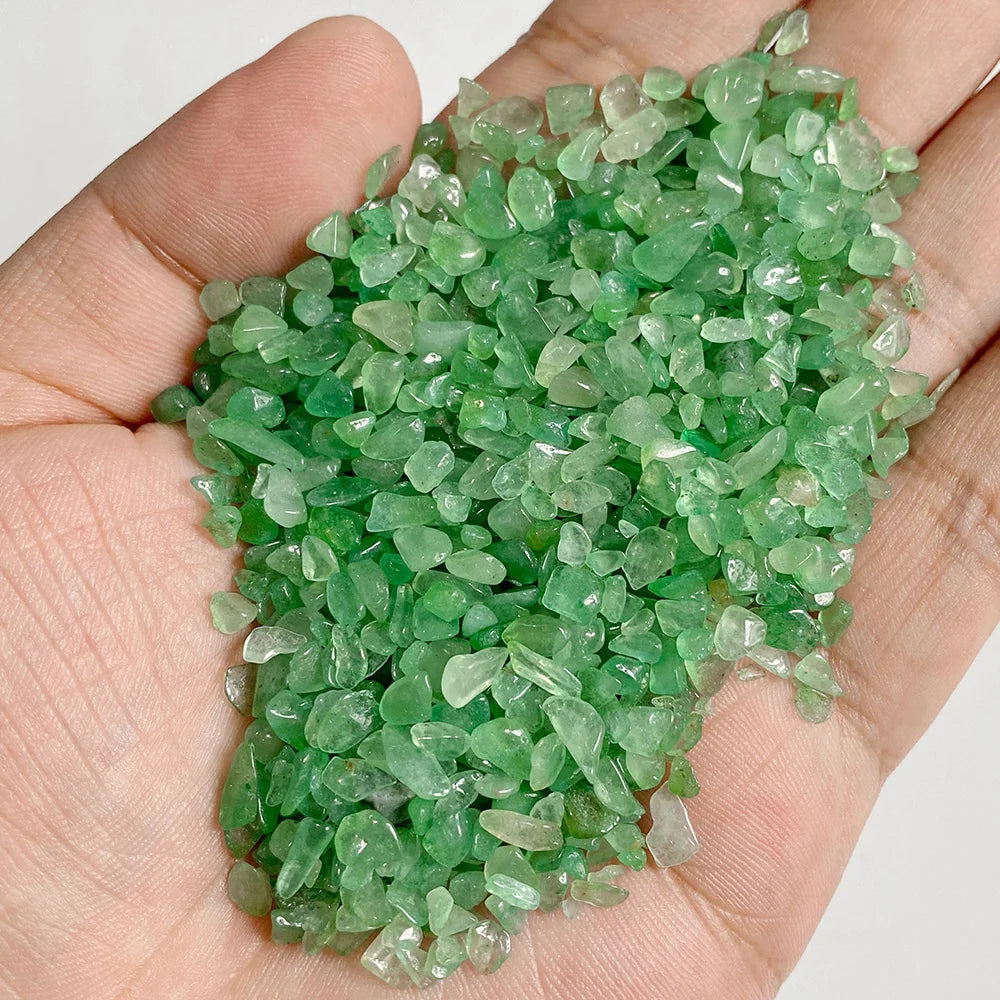 A hand holds a pile of bright green natural tumbled stone chips for jewelry making and home decor.