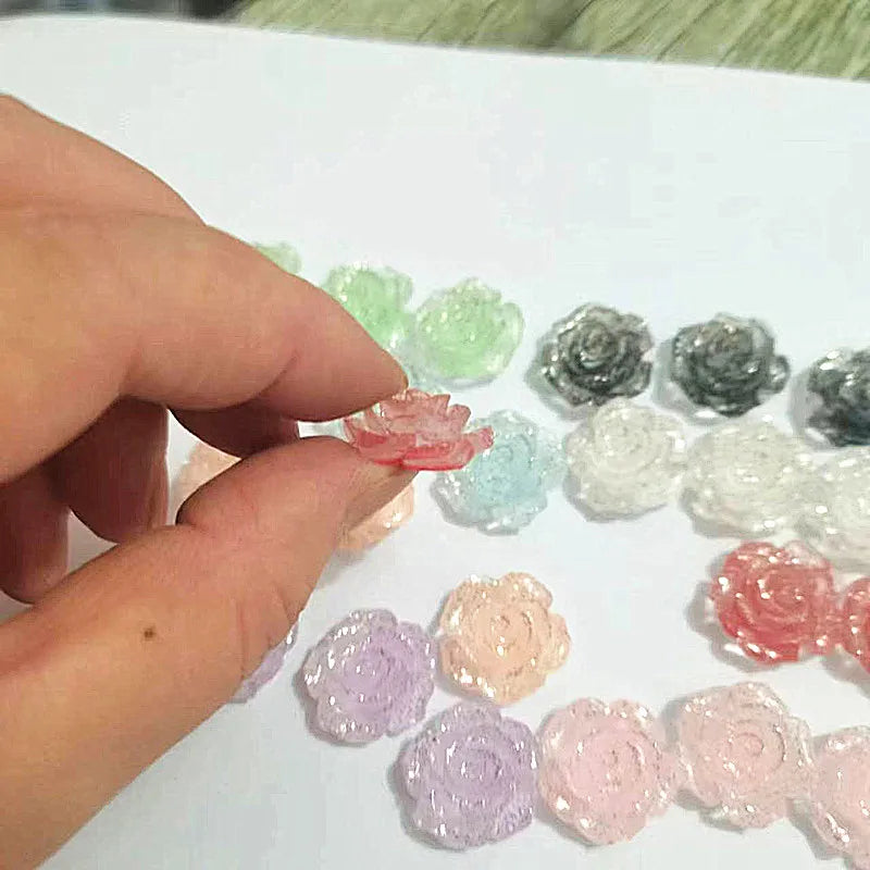 A hand is holding and arranging a variety of pink, green, and white resin flatback flowers for DIY crafts.