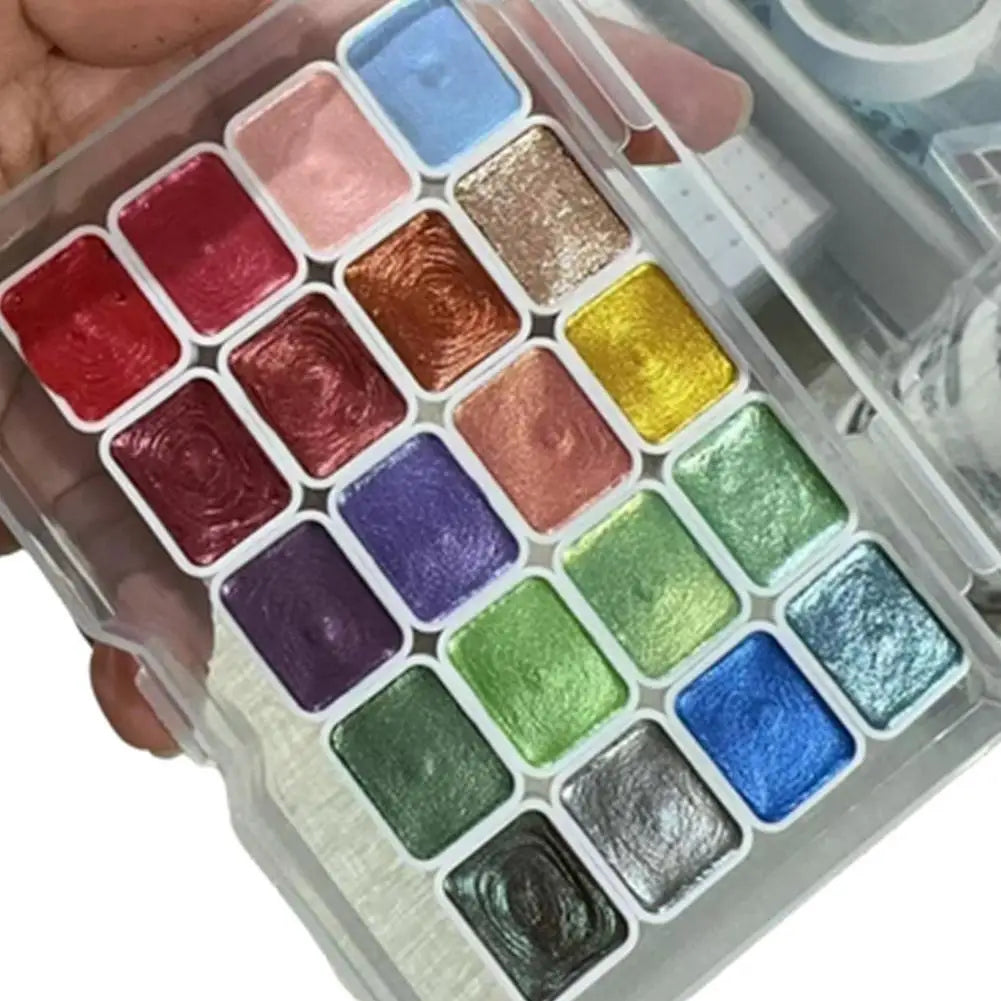 A collection of 20 watercolor paint colors in a clear plastic tin arranged in a grid.