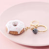 A white crochet donut keychain pendant with pink accents and a gold-colored ring.