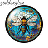 A round glass cabochon featuring a detailed bee design with yellow and black stripes and surrounding floral elements.