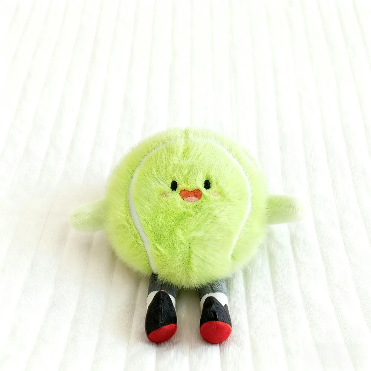 A soft lime green plush sports ball with black and red accents resting on a white surface.