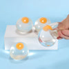 A hand holds a clear, squishy hamburger stress ball with an orange top, resting on a white surface.