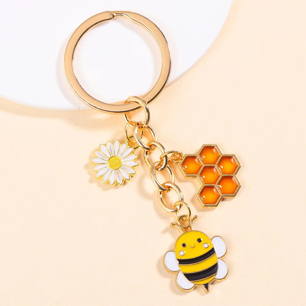 Gold-toned keychain featuring a daisy flower and a bee enamel charm on a white background.