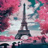 A vibrant pink tree frames the Eiffel Tower under a cloudy sky, with a bridge and water in the foreground.
