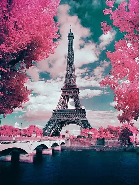 A vibrant pink tree frames the Eiffel Tower under a cloudy sky, with a bridge and water in the foreground.