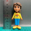 A playful cartoon PVC figurine of a girl with brown hair, wearing a yellow shirt and blue pants.