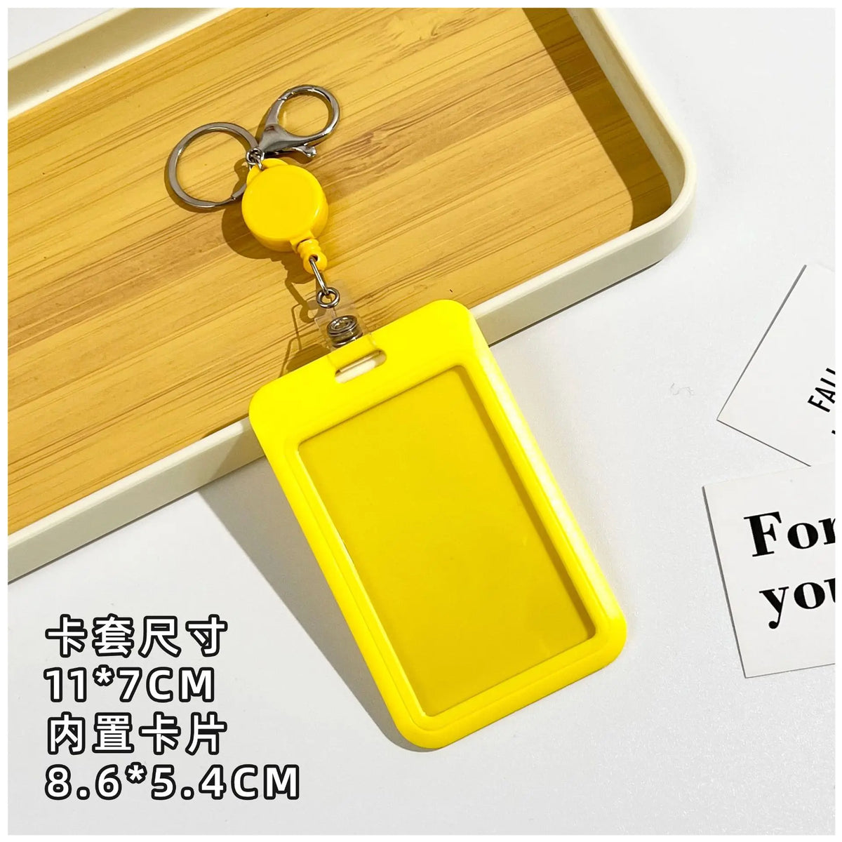 Yellow plastic ID badge holder with a keychain attached, shown resting on a wooden tray.
