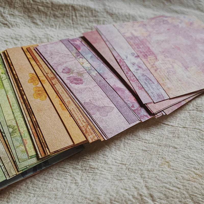 A stack of rainbow textured paper sheets in various shades of pink, purple, and yellow lying on a light fabric.