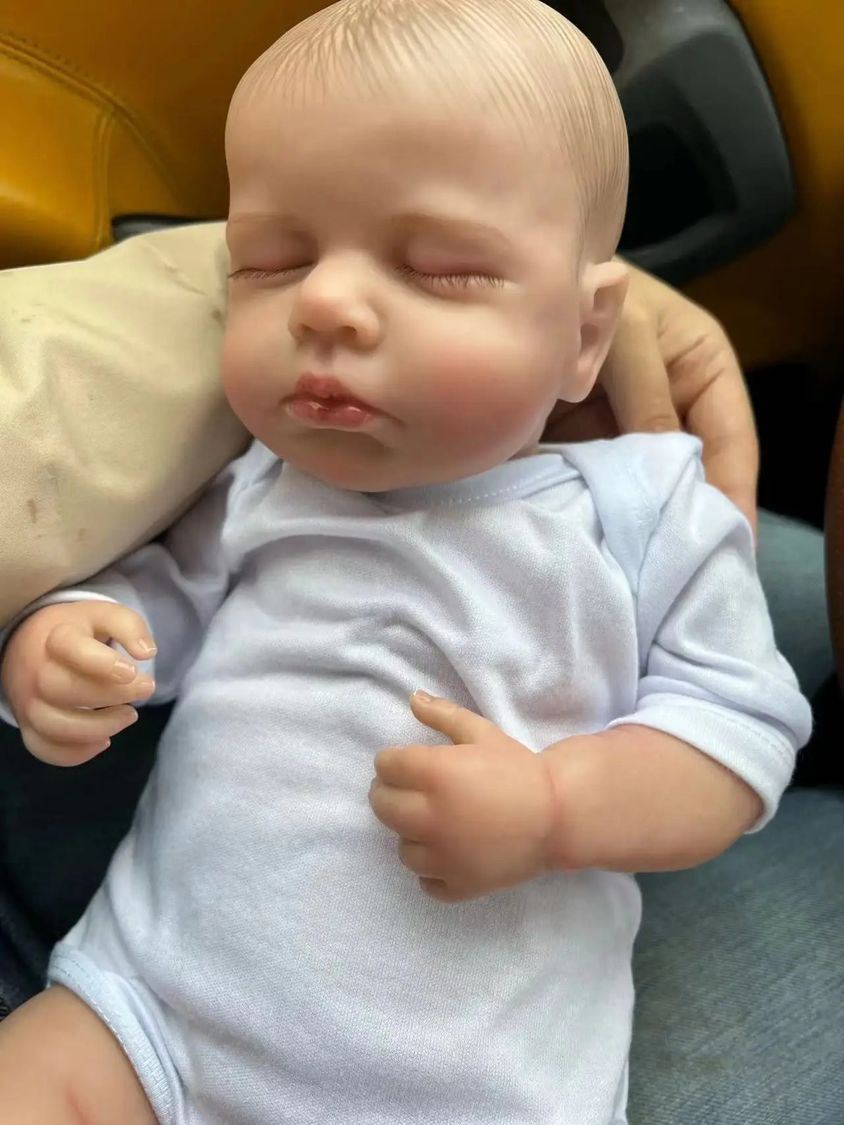 A realistic reborn baby doll with a light blue cloth body is shown in a close-up shot.