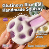 A hand holds a white glutinous rice ball handmade squishy toy with purple accents, demonstrating its moldable texture.