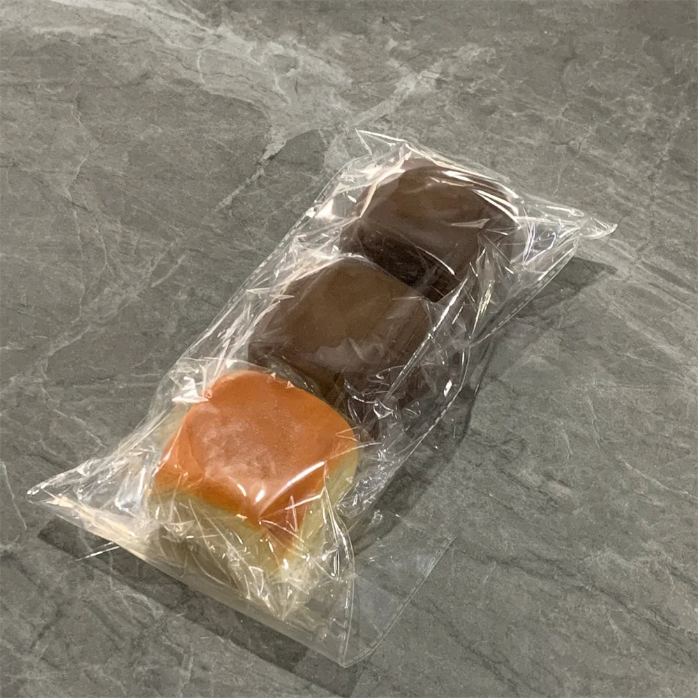 Trois petits pains décoratifs en tissu doux de couleur marron et orange, emballés dans du plastique transparent.