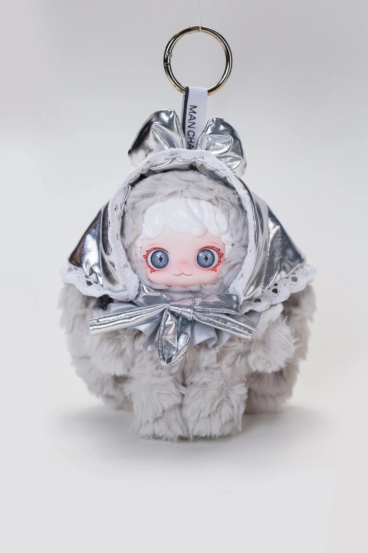 A silver-wrapped blind box plush doll with white hair and blue eyes, tied with a bow, hanging from a keyring.