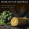 A bundle of natural beeswax taper candles is shown next to green foliage.
