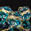A close-up of a set of resin dice with golden elven numbers and blue-green translucent material.