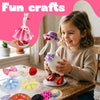 A young girl is holding a white goose figurine costume set with pink accents and various accessories on a wooden table.