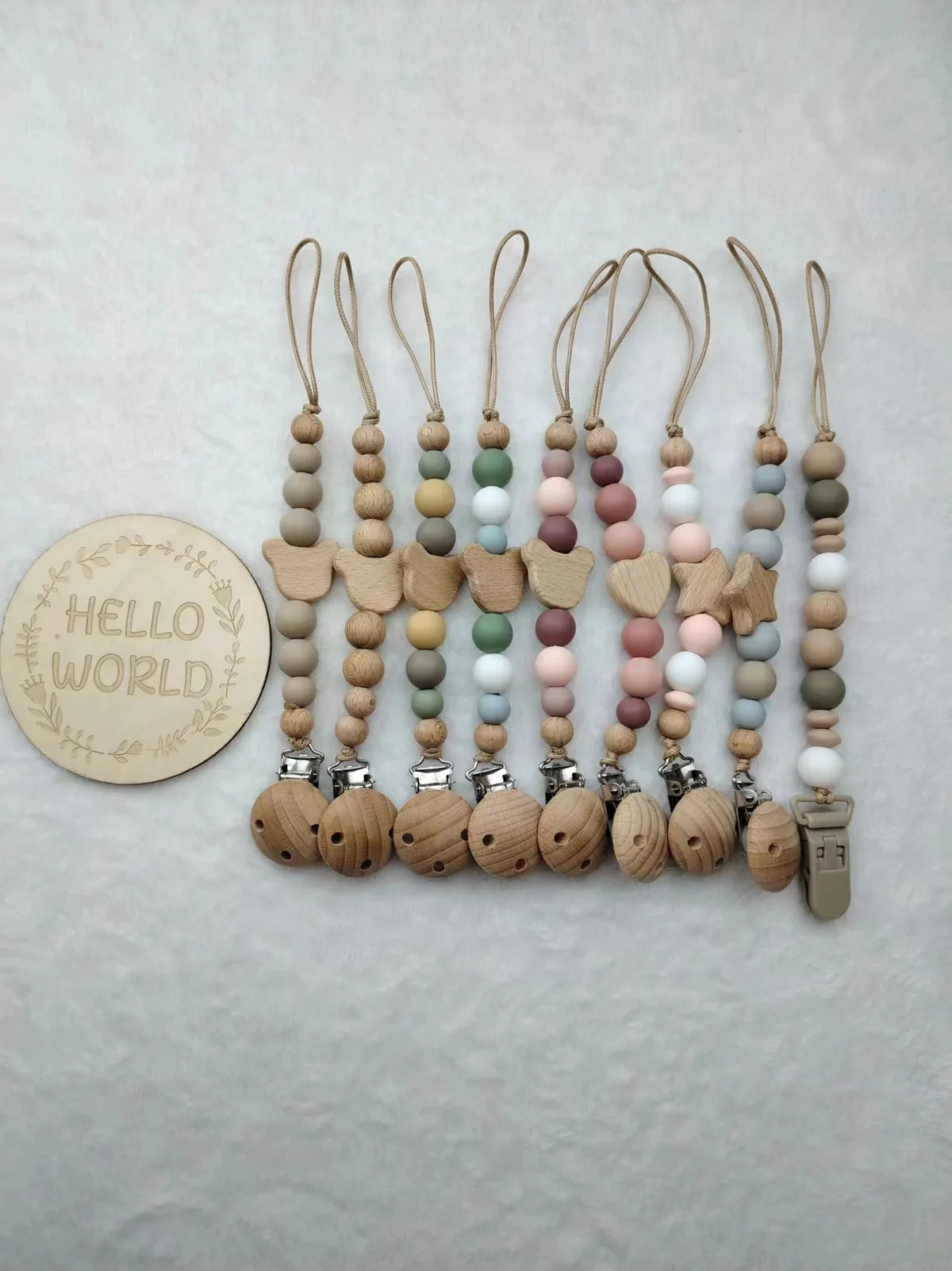 A string of personalized wooden baby pacifier clips featuring silicone beads in various natural and pastel colors.