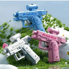 A pink and blue prank gun toy is shown lying on green grass with foliage in the background.
