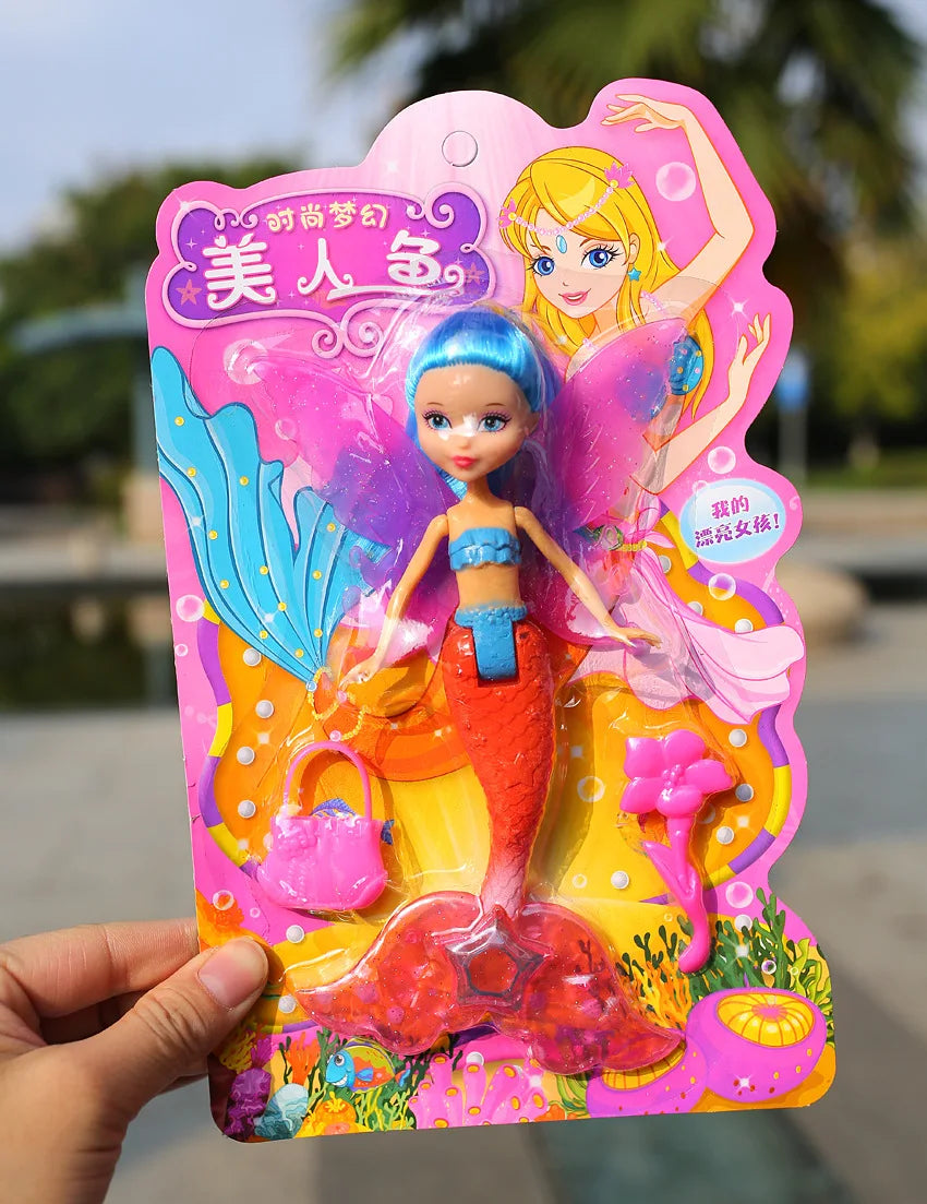 A pink and yellow mermaid princess doll with blue hair and orange tail is held in a hand.