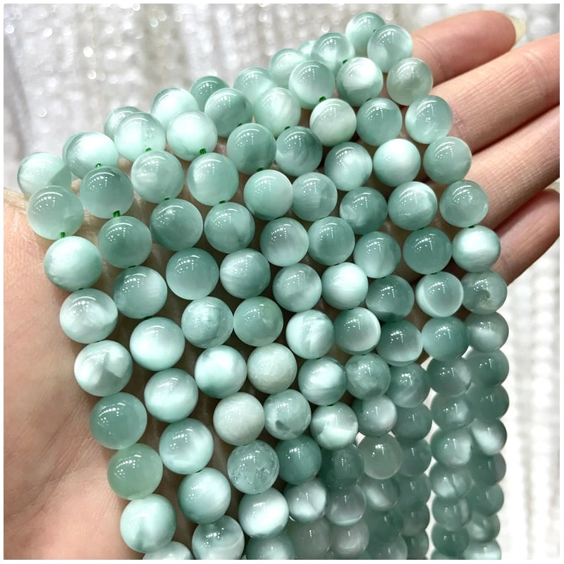 A hand holds a strand of light blue-green natural stone beads for DIY jewelry making