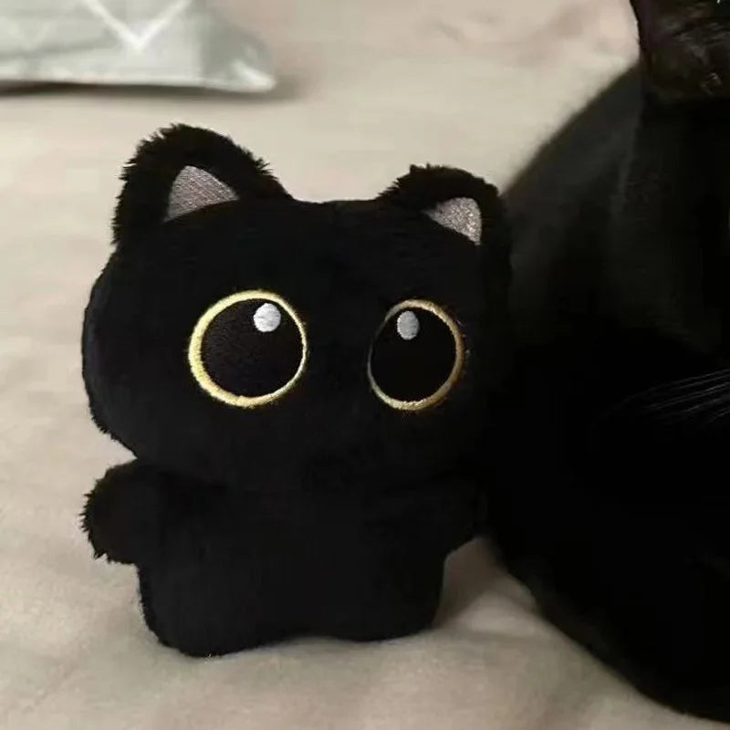 A close-up of a black cat plush cushion with large gold eyes resting on a light surface.