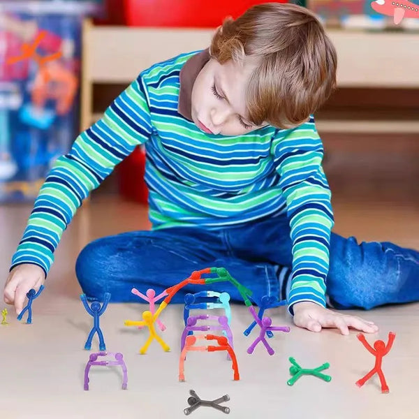 A child is playing with colorful magnetic humanoid toys scattered on a light wooden surface.