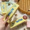 A yellow butter stick squishy toy is shown next to a plate and a woven basket.