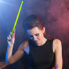 A woman holds a bright green glow-in-the-dark nylon drumstick against a dark, smoky background.