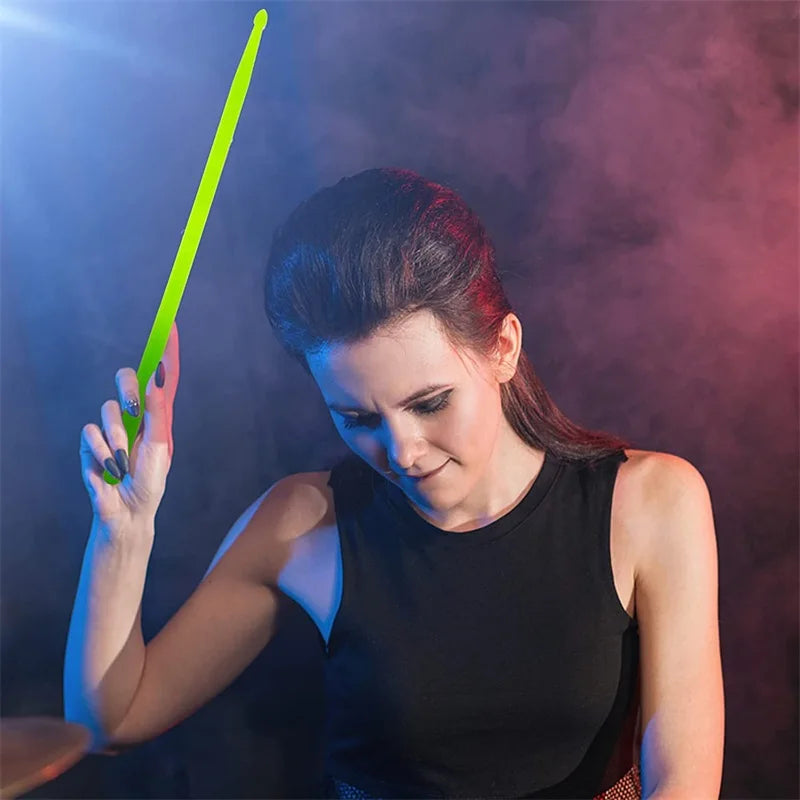 A woman holds a bright green glow-in-the-dark nylon drumstick against a dark, smoky background.