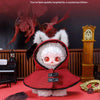 A fluffy red hooded plush doll with white hair and large eyes sits on a red surface.
