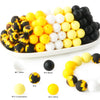 A collection of soft food-grade silicone beads in yellow, white, and black colors arranged on a white platter.