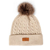 Beige knit winter hat with a faux fur pom and a leather tag for jeans
