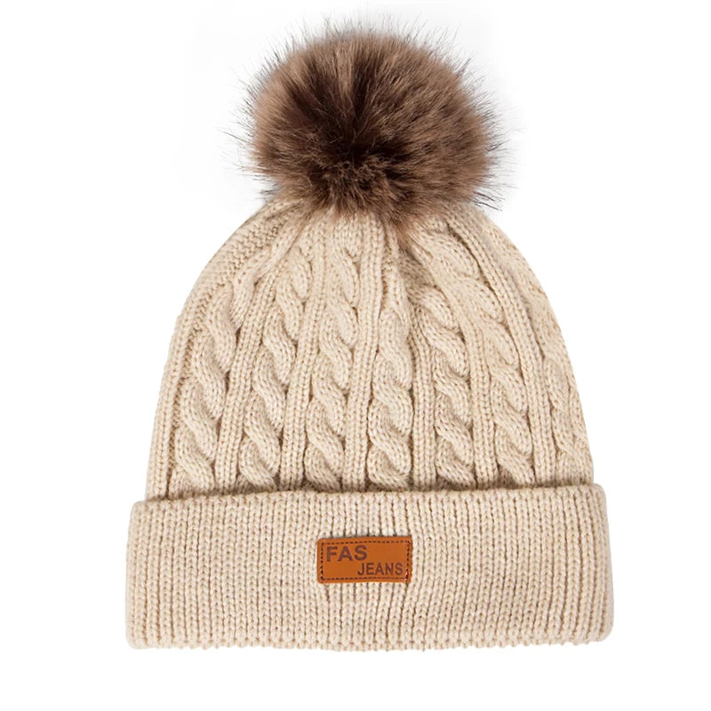 Beige knit winter hat with a faux fur pom and a leather tag for jeans