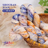 A bundle of hand-dyed wool yarn in blue, orange, and white gradients is displayed in a woven basket.