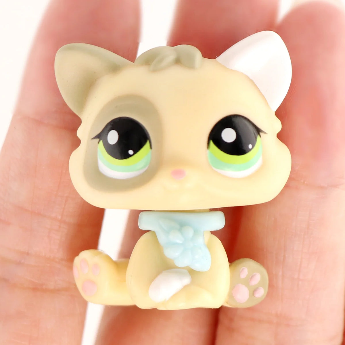 A small, light yellow miniature cat figure with white ears and blue accents is held in a person's hand.
