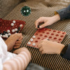Hands are playing with a large 100-sided acrylic polyhedral die and small white and red beads on a striped fabric.