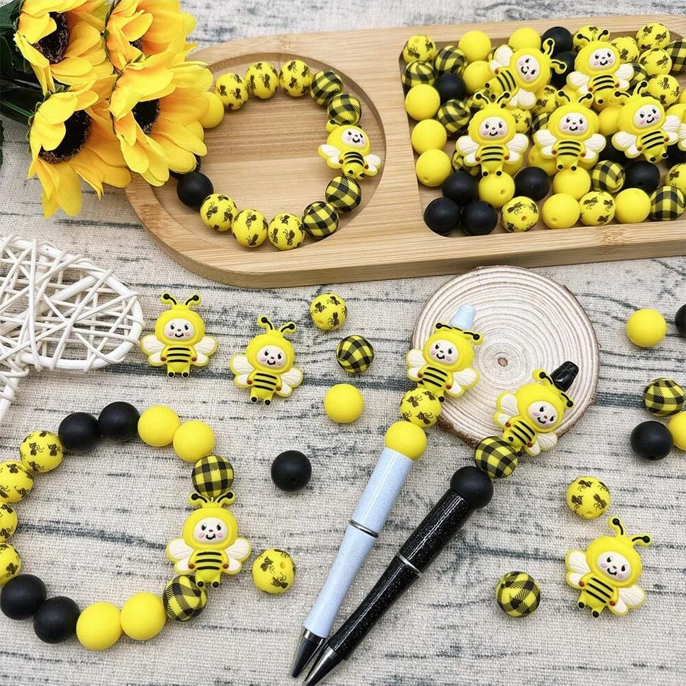Yellow and black silicone bee beads arranged on a wooden board with yellow sunflowers and craft tools.