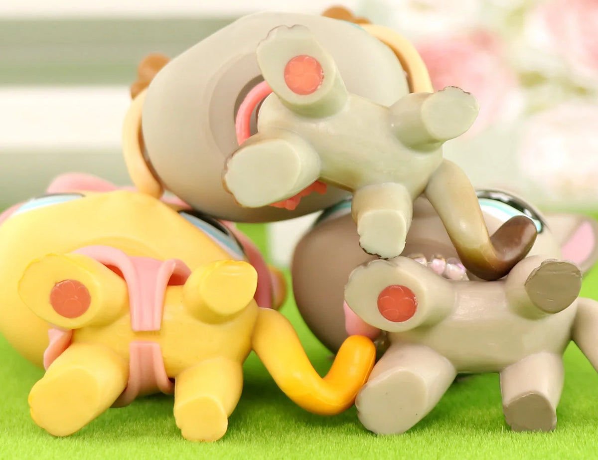 A set of three pastel-colored vinyl cat figurines with pink scarf necklace accessories displayed on green moss.