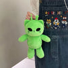 A bright green plush toy shaped like an alien cat is being held by a person wearing a denim apron.