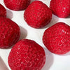 A close-up view of several bright red strawberry squishy toys resting on a white surface.