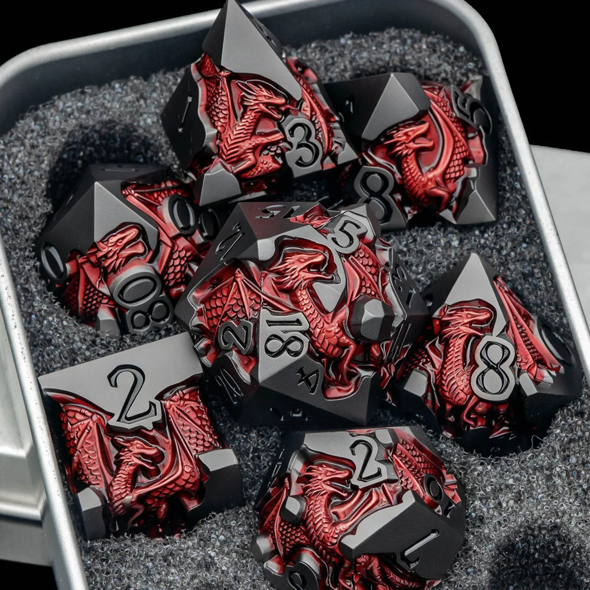 A set of black metal dice featuring a red dragon design is displayed in a silver container.