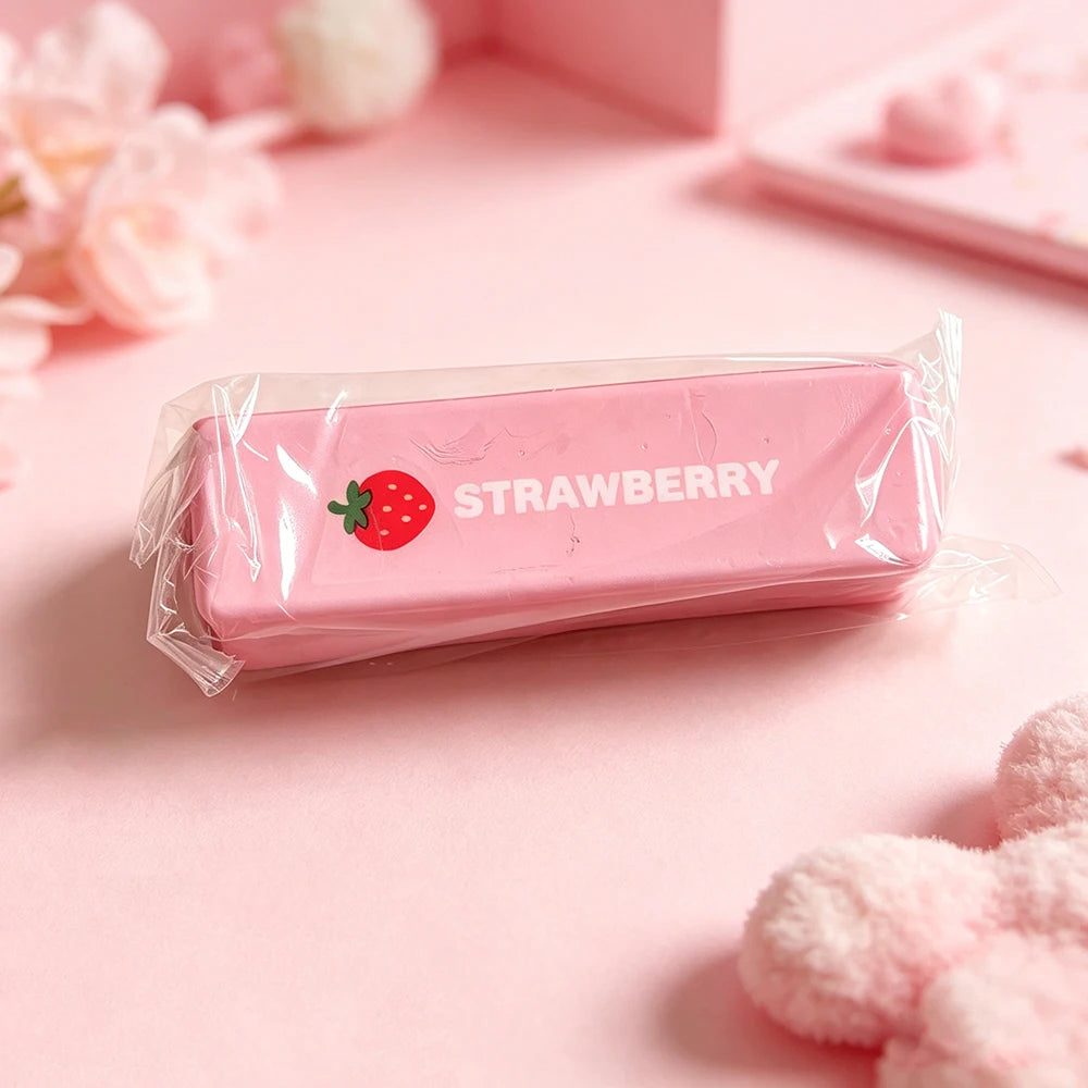 A pink strawberry-themed squishy toy is packaged in a clear plastic bag on a light pink surface.