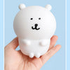 A white silicone lamp shaped like a bear with black facial features is held in a hand.