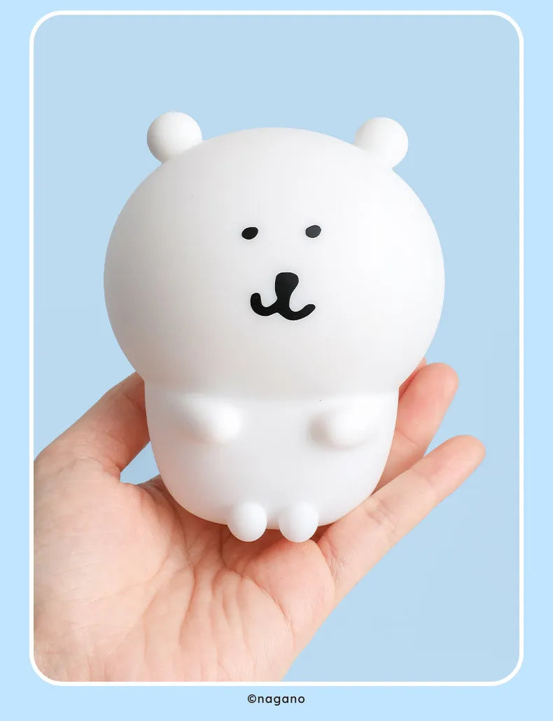 A white silicone lamp shaped like a bear with black facial features is held in a hand.