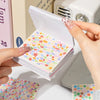 A hand holds open a stack of Star Storm Mini Deco Cut Film Sticker Book for scrapbooking and DIY crafts with colorful pattern