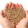 A hand holds a pile of round gold spacer beads for DIY jewelry making